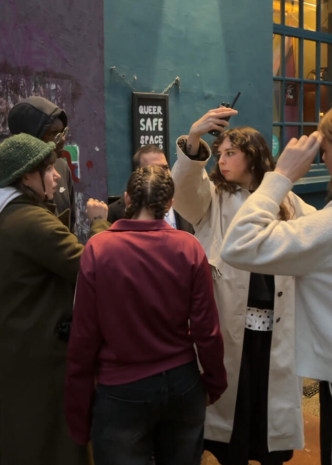 A Group of people outside. One pointing holing a walkie talkie